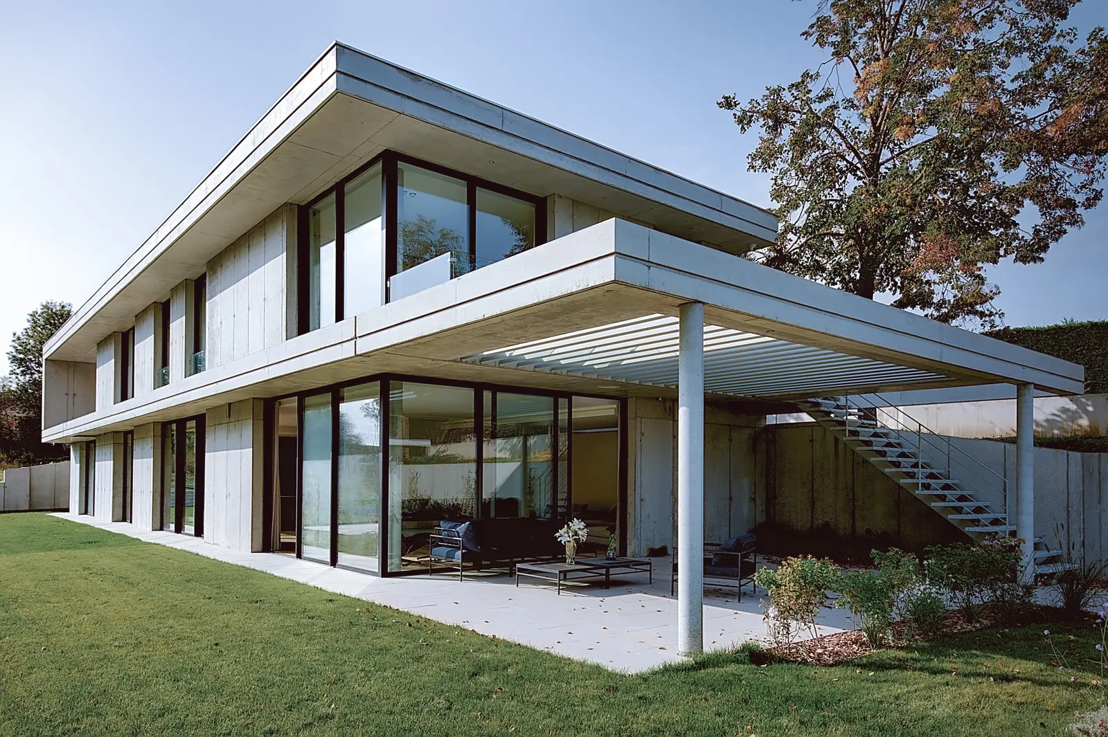 Maison en béton banché de Tassin vue depuis le jardin, terrasse couverte et salon extérieur sous la dalle