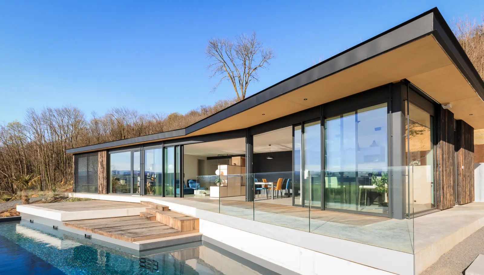 Maison ossature bois de plain-pied dans la pente à Beausemblant, larges baies vitrées ouvertes sur les terrasses et le bassin de nage