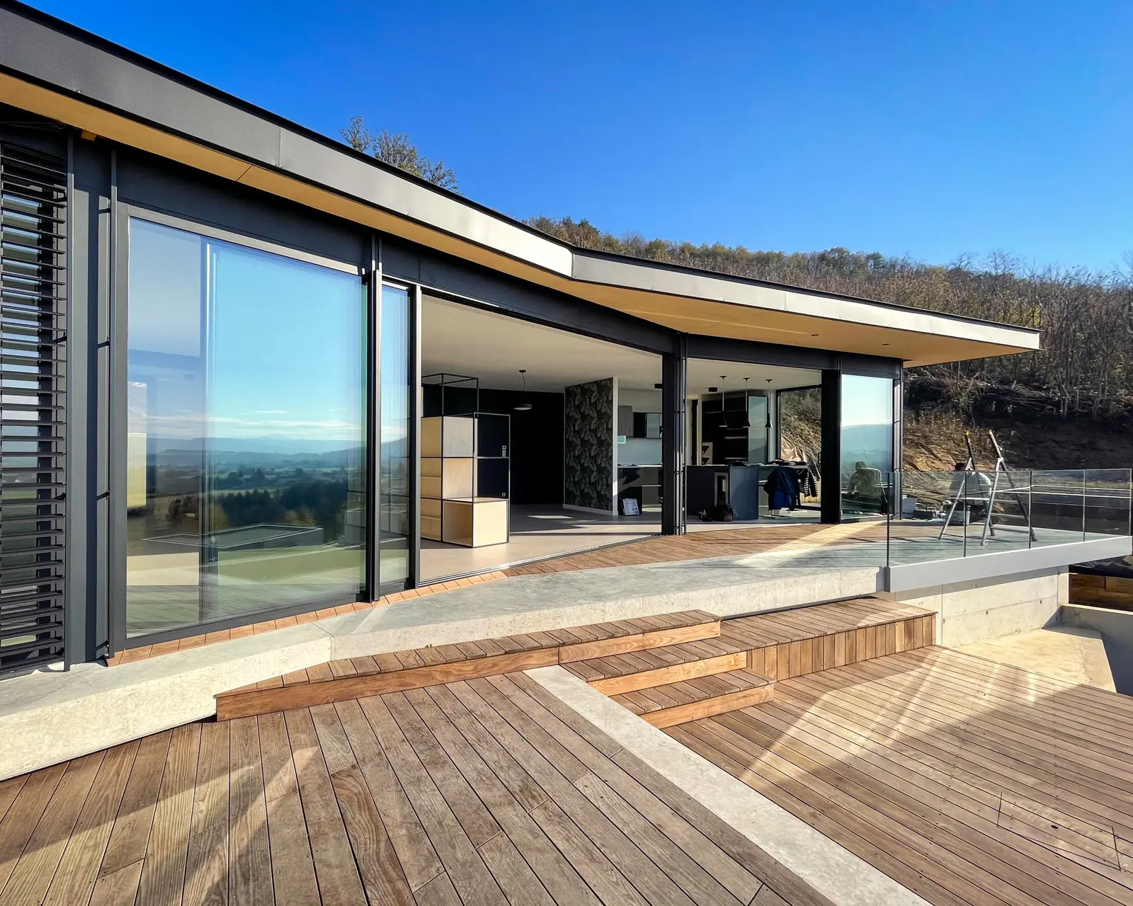 Façade vitrée de la maison ossature bois dans la pente, larges baies ouvertes sur le paysage drômois