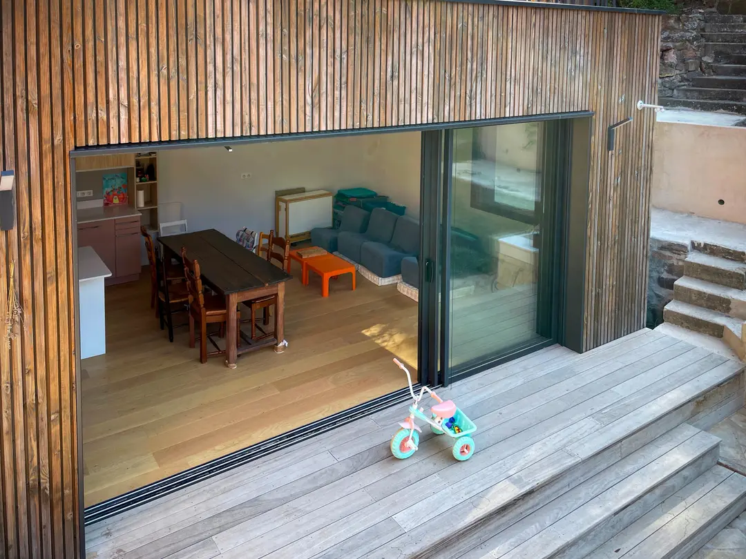 Extension en ossature bois à Cannes, baie coulissante entièrement ouverte sur la terrasse bois, pièce de vie traversante