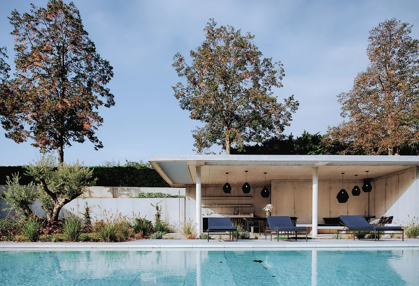 Pool house en béton de la maison de Tassin, cuisine d'été et bains de soleil au bord de la piscine