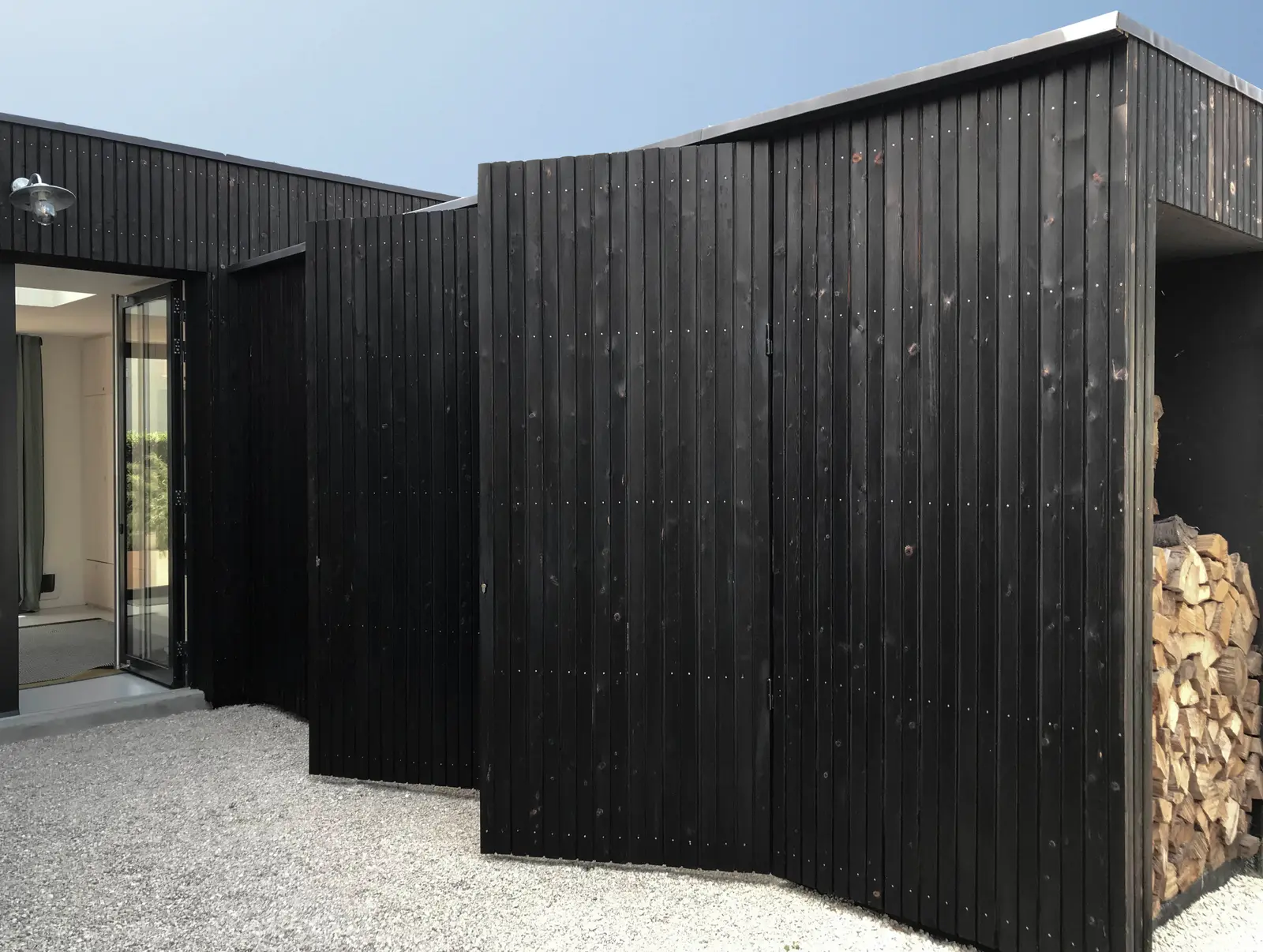 Extension en bois brûlé, portes et rangements fondus dans le bardage, abri à bûches intégré