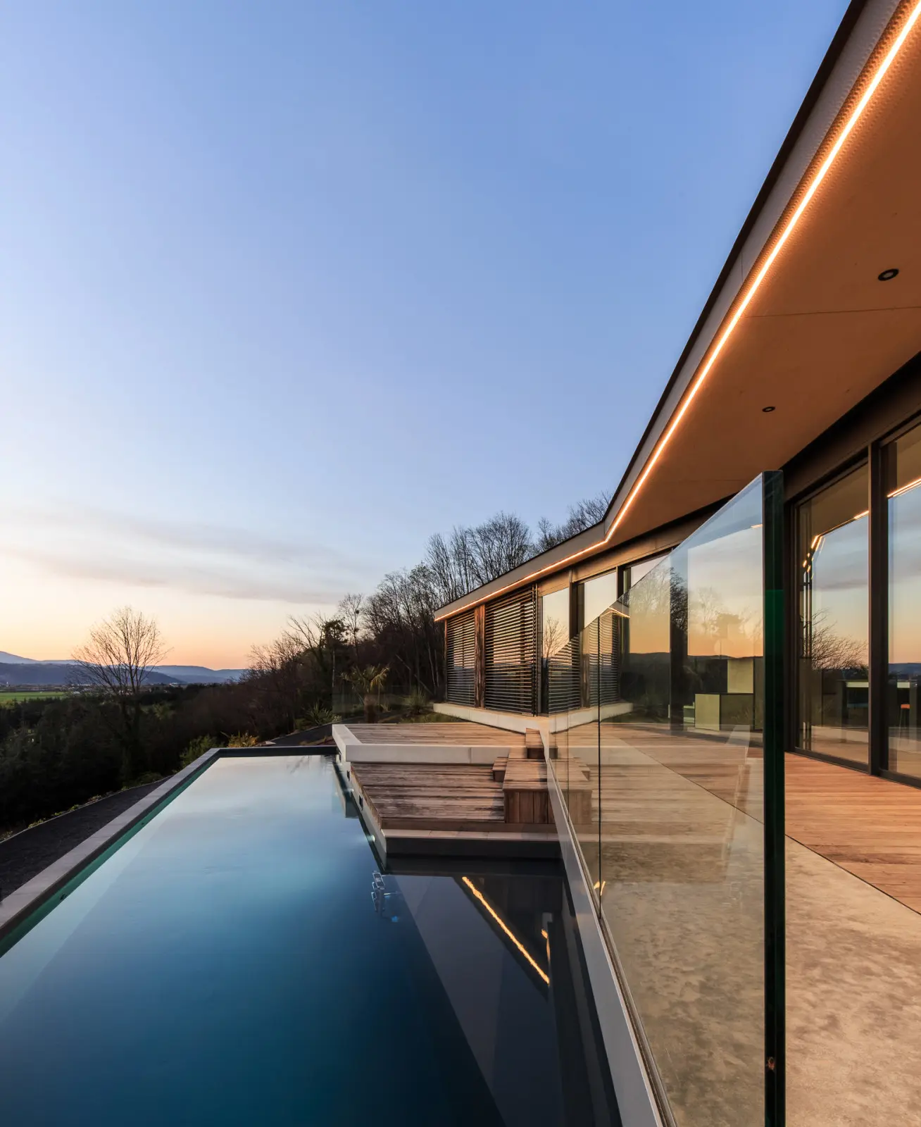 Maison ossature bois dans la pente au crépuscule, façades éclairées